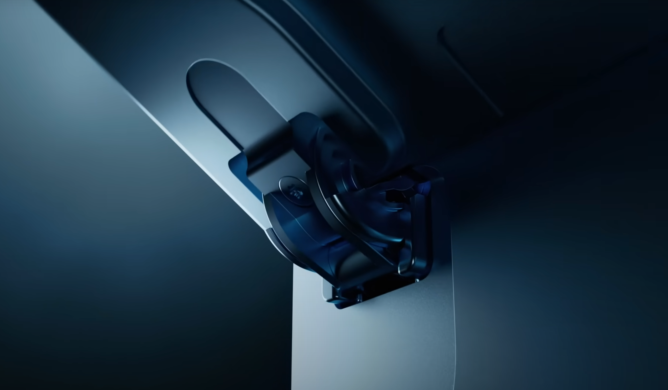 Close-up of a metal hinge mechanism attached to a sleek, dark surface, illuminated by blue lighting. The hinge has an angular design, and the surface appears to be part of a larger, modern device or appliance.