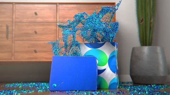 Two gift bags on the floor, one smaller and solid blue, the other larger with a blue and green circular pattern. Both bags are overflowing with blue glittery streamers, with more scattered around them. A wooden dresser and a large potted plant are in the background.