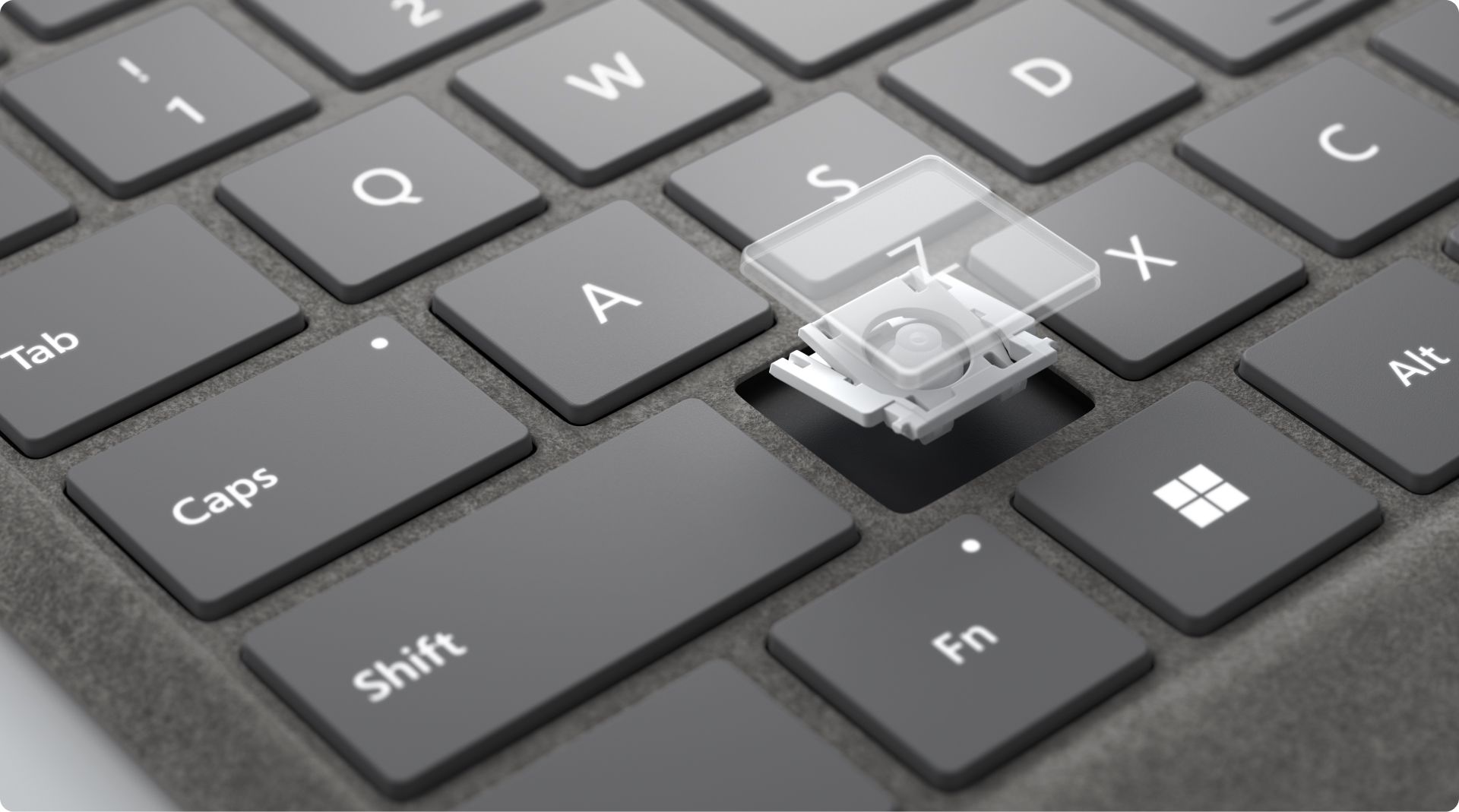 Close-up of a keyboard with the "A" key removed, revealing the key mechanism underneath. The surrounding keys, including "Tab," "Caps," "Shift," "Fn," "Alt," "X," "S," and "Z," are visible. The keyboard has a sleek design and a soft material base.