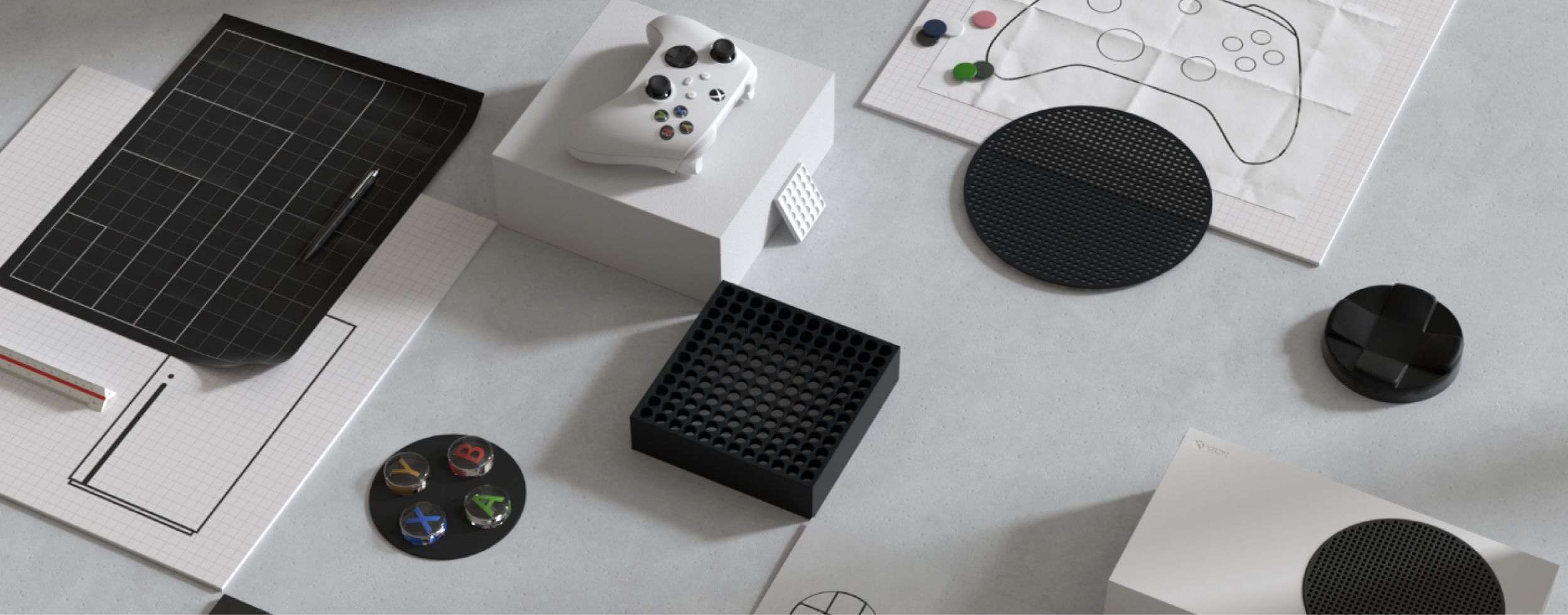 Top view of various gaming console accessories and components arranged on a plain surface. Items include a white gaming controller, a black and white console component, a black grid-like block, and coasters with colorful designs.