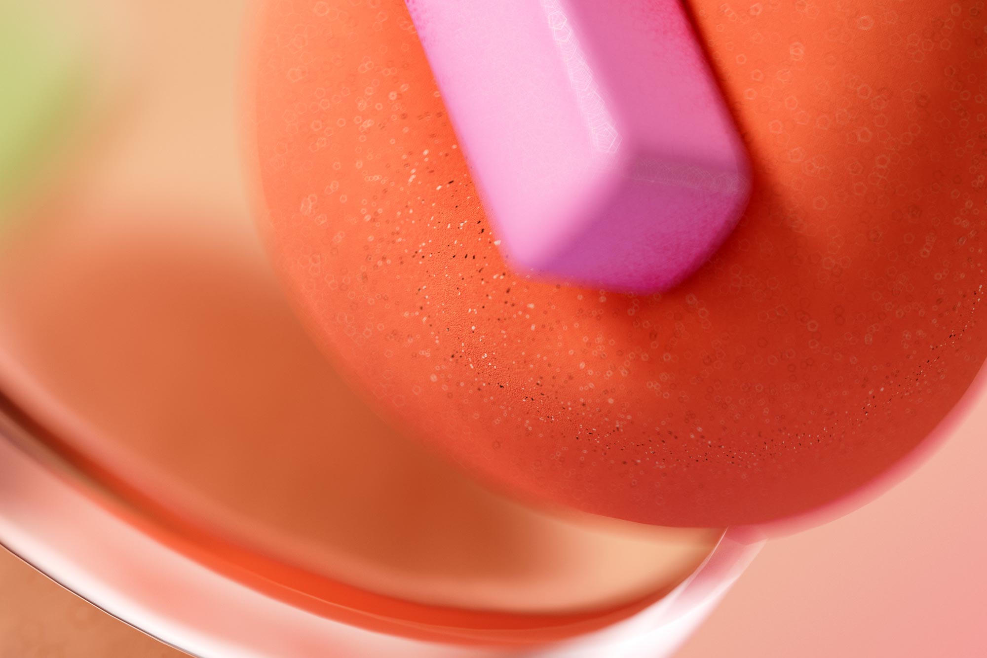 Close-up of a vibrant orange sphere with a smooth, glossy texture and tiny dotted details. A pink, geometric shape, possibly a chalk or clay piece, rests on top. The background features blurred shades of peach and green, creating a soft and colorful backdrop.