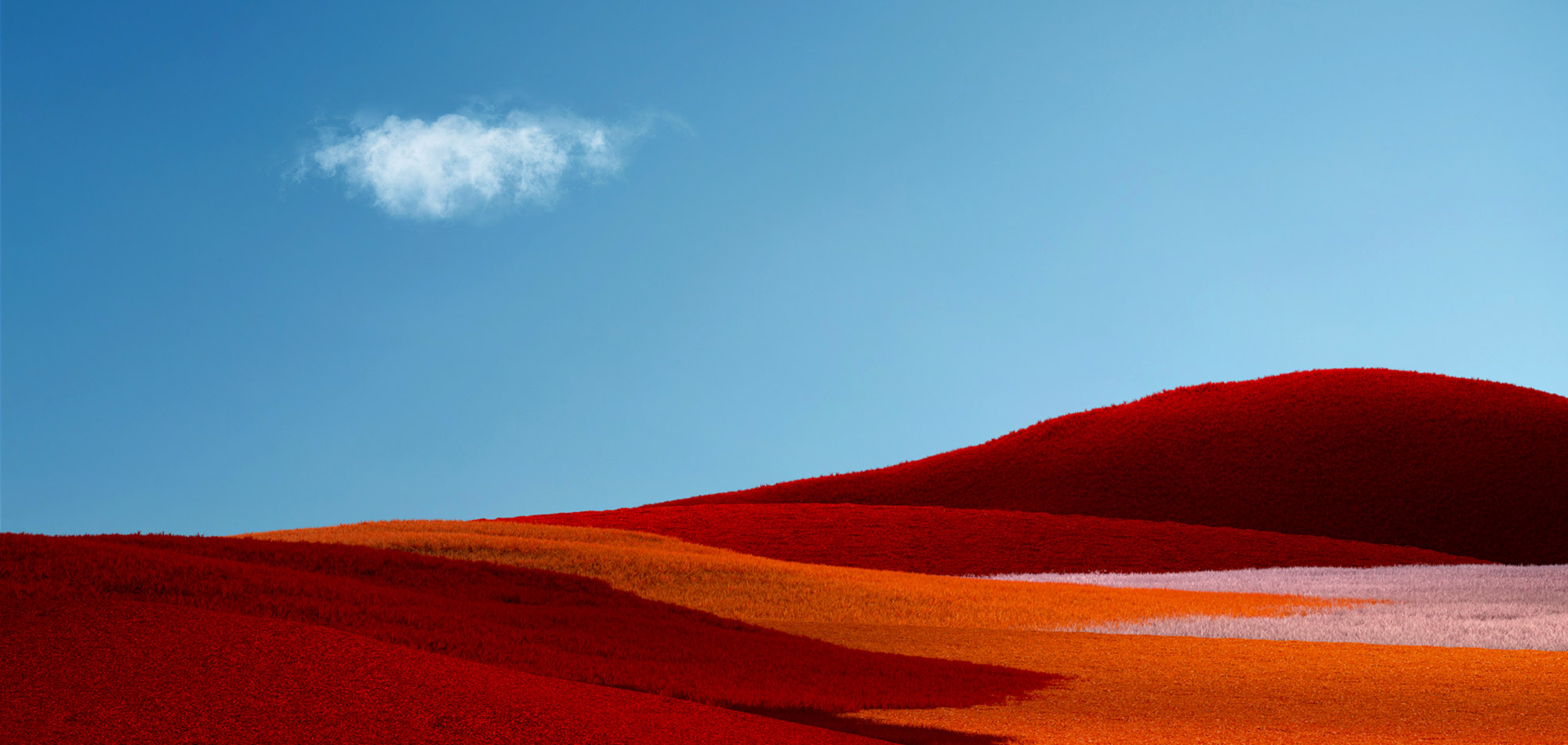 A minimalist landscape features rolling hills in vibrant red, orange, and pink hues under a clear blue sky. A single small white cloud hovers in the upper left corner, creating a striking contrast with the colorful scenery below.