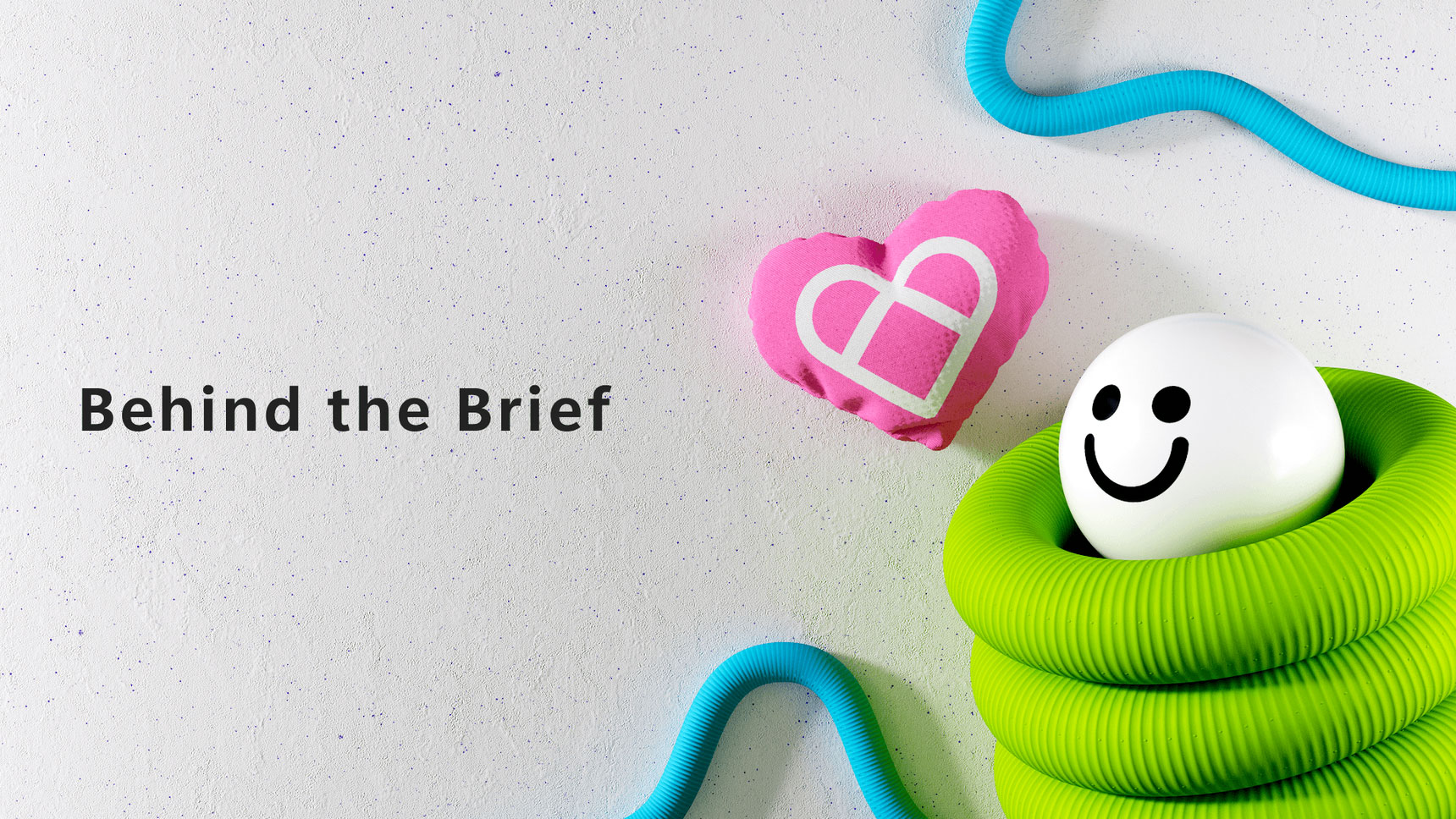 Image featuring a white background with text reading "Behind the Brief" on the left. On the right, a smiley face ball is partially wrapped in a green flexible tube, next to a pink heart object containing a white geometric shape. Blue tubes frame the top right corner.