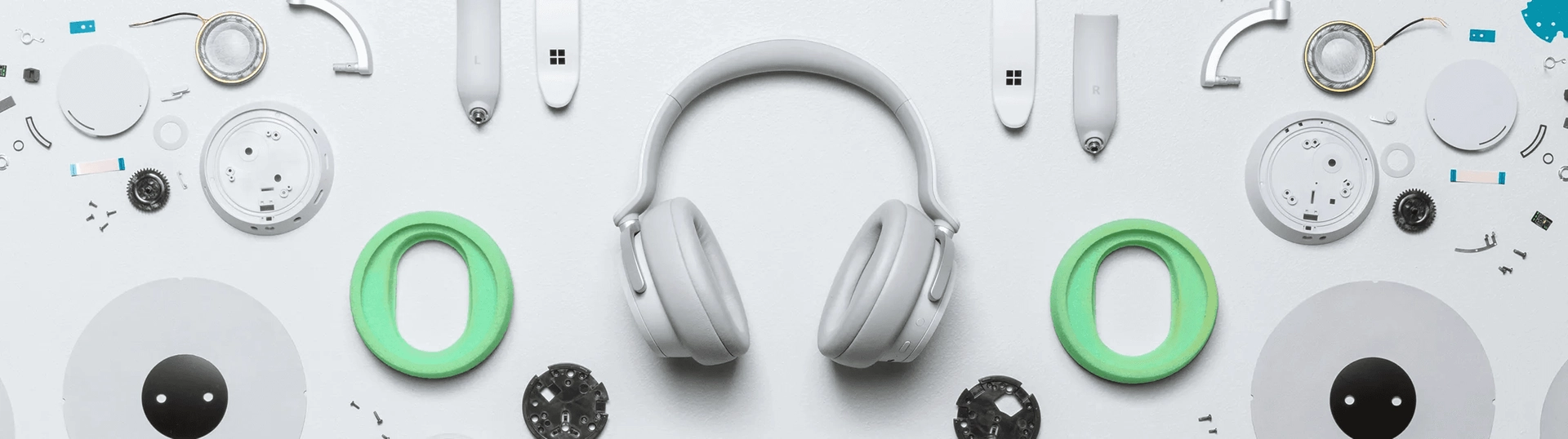 A pair of white over-ear headphones is centered on a white background, surrounded by an assortment of disassembled headphone parts, including ear cushions, wires, and circular components, all meticulously laid out in a symmetrical pattern.