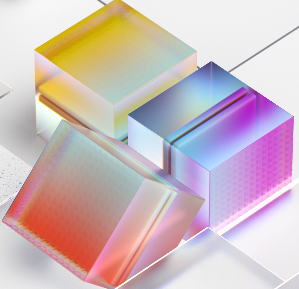 Three translucent, multicolored cubes with a holographic appearance rest on a reflective white surface. The cubes are arranged in an informal cluster, displaying a blend of yellow, pink, and blue shades with subtle geometric patterns.