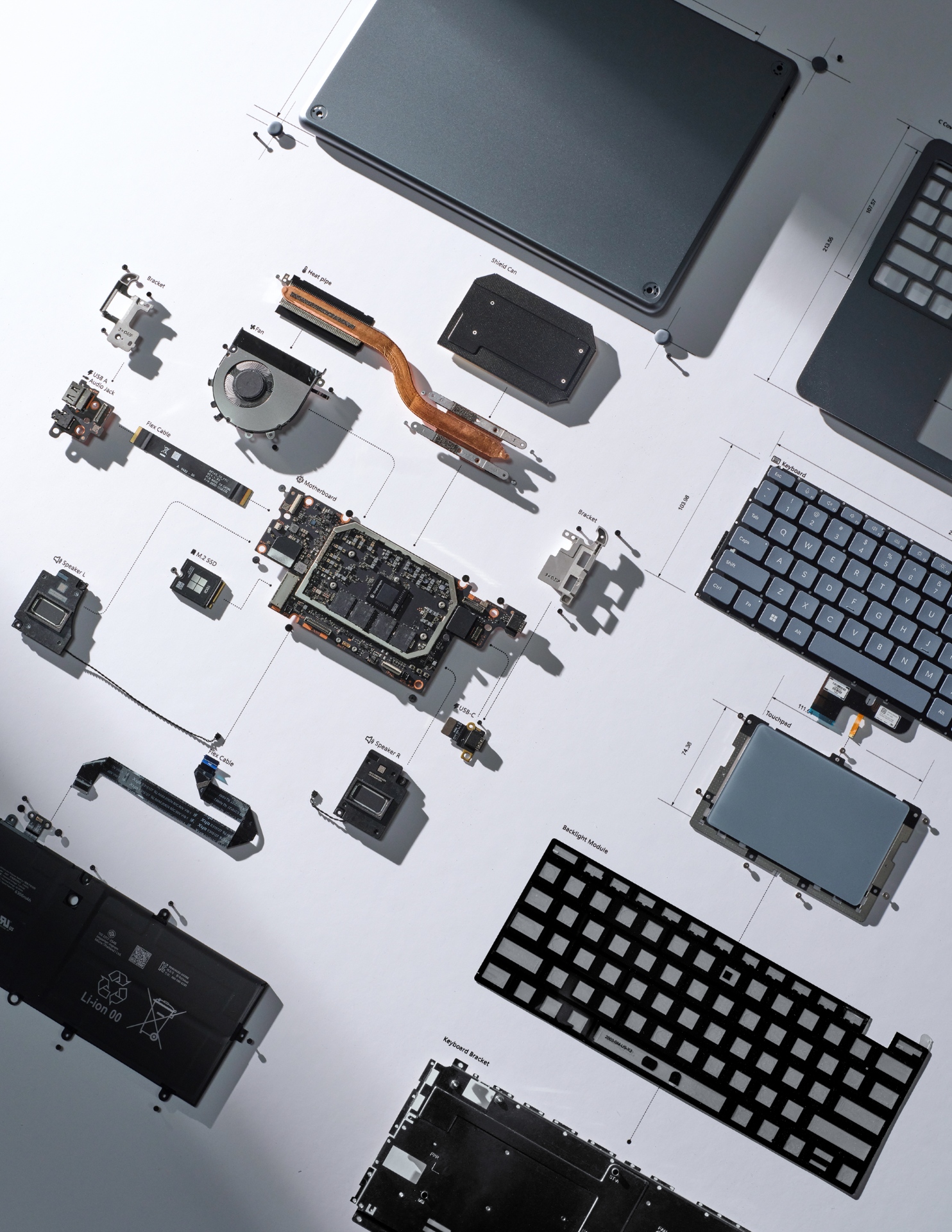 An overhead view of a disassembled laptop with its components, including the keyboard, battery, trackpad, fan, and circuit boards, neatly laid out on a white surface with labeled diagrams.