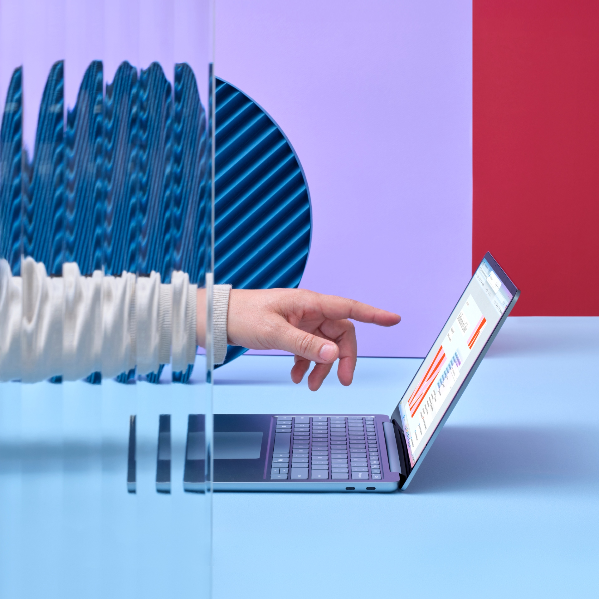 A hand extends through a glass panel, pointing at a laptop displaying graphs and charts on a colorful background with red, purple, and blue geometric shapes.