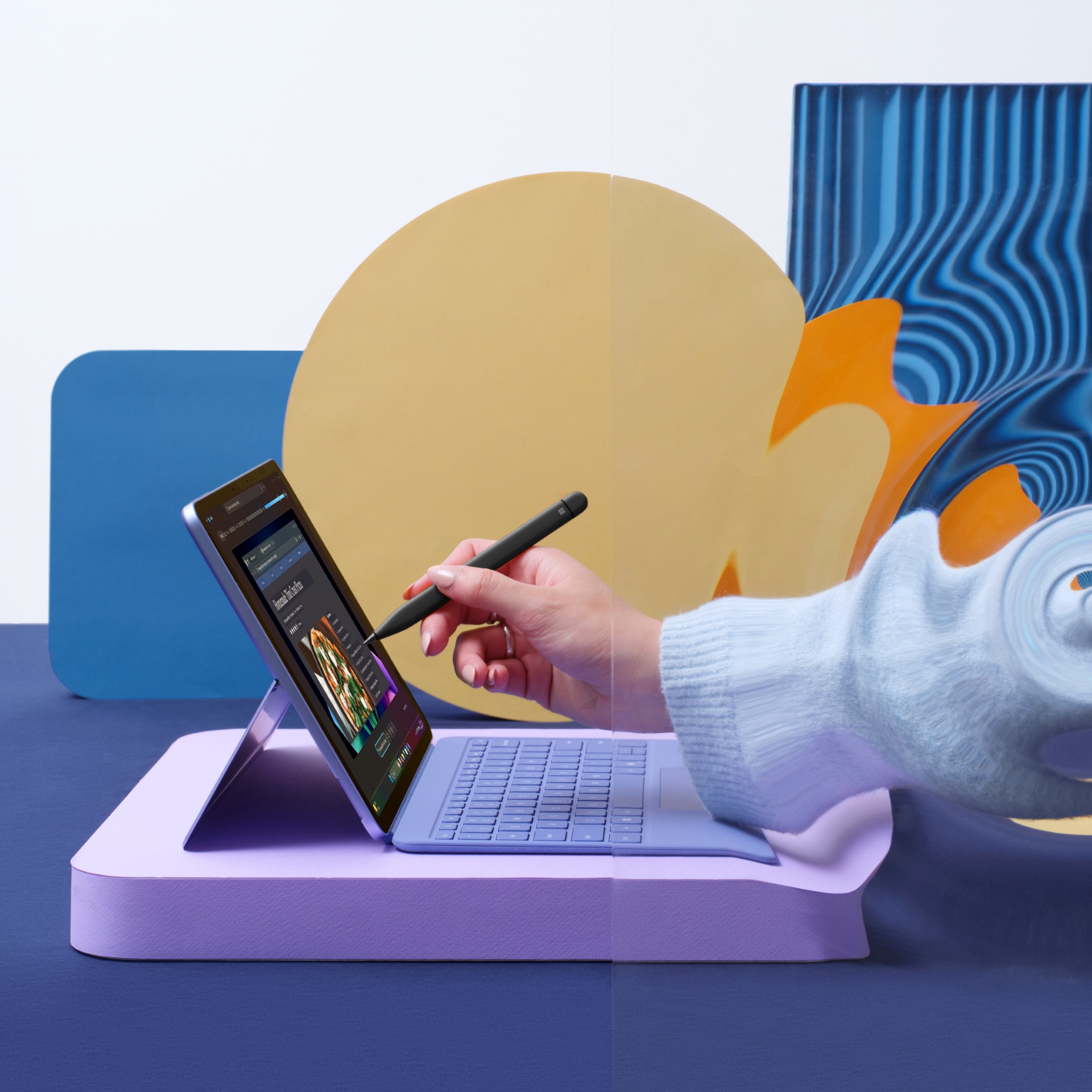 A person uses a stylus to interact with a tablet on a purple stand, surrounded by colorful abstract shapes and backgrounds in blue, yellow, and orange tones.