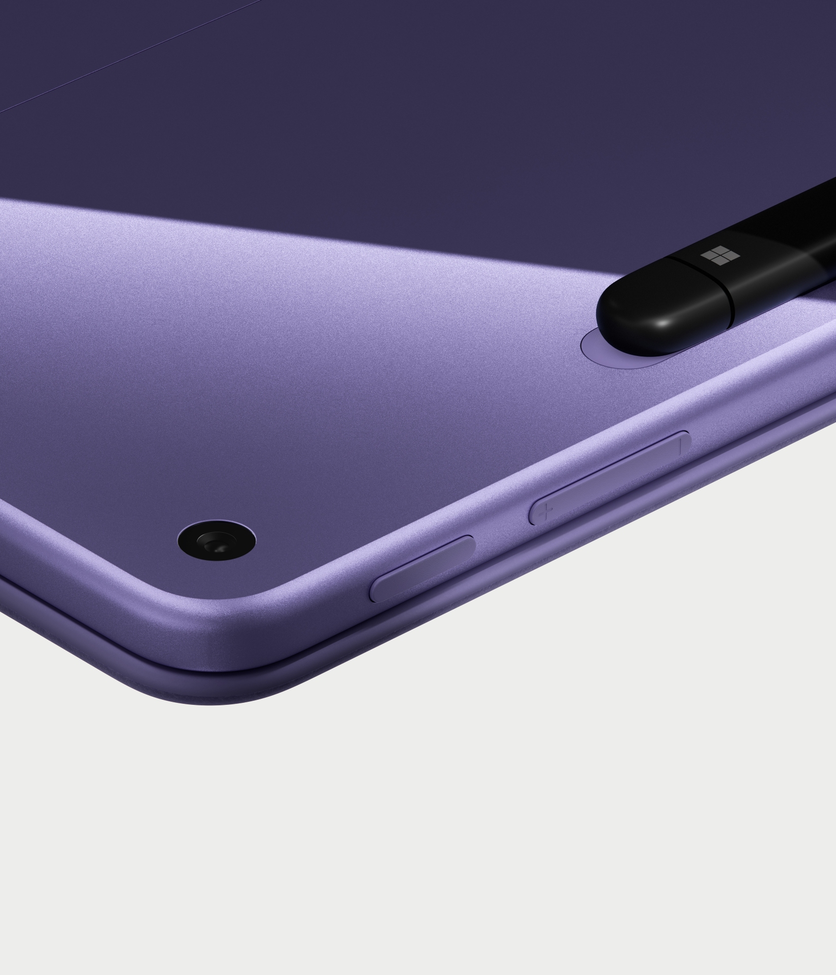 Close-up of the corner of a purple tablet with a camera lens, volume buttons, and a black stylus attached magnetically to the edge on a light background.