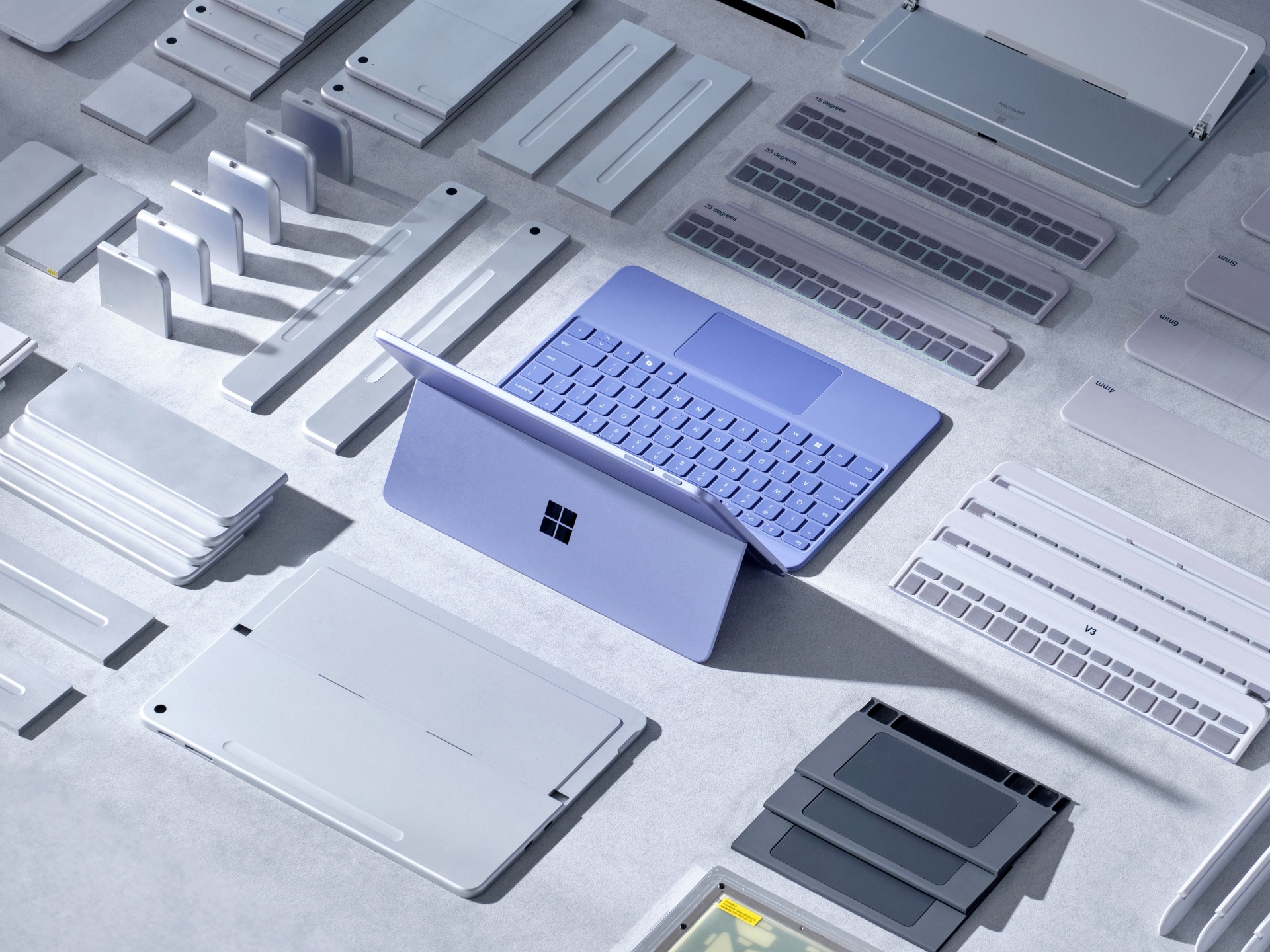 A blue Microsoft Surface laptop is surrounded by various electronic device components and accessories, all neatly arranged on a light grey surface. The laptop is open, highlighting its keyboard and sleek design.