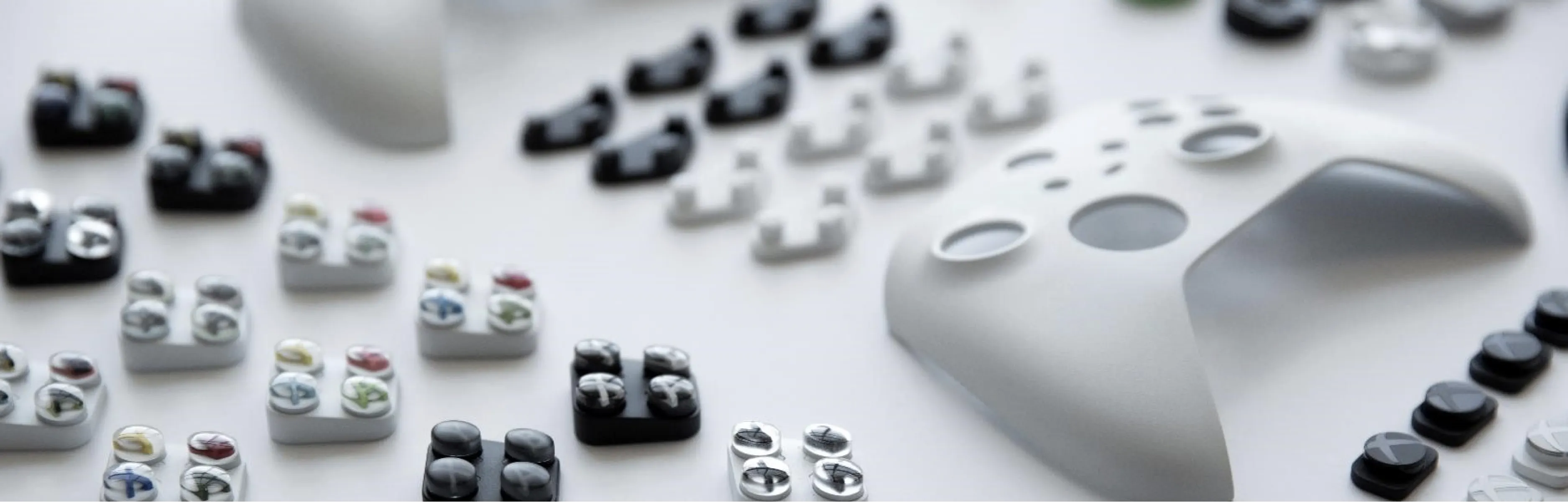 A close-up of several disassembled white game controllers and various colored buttons arranged in neat rows on a white surface.