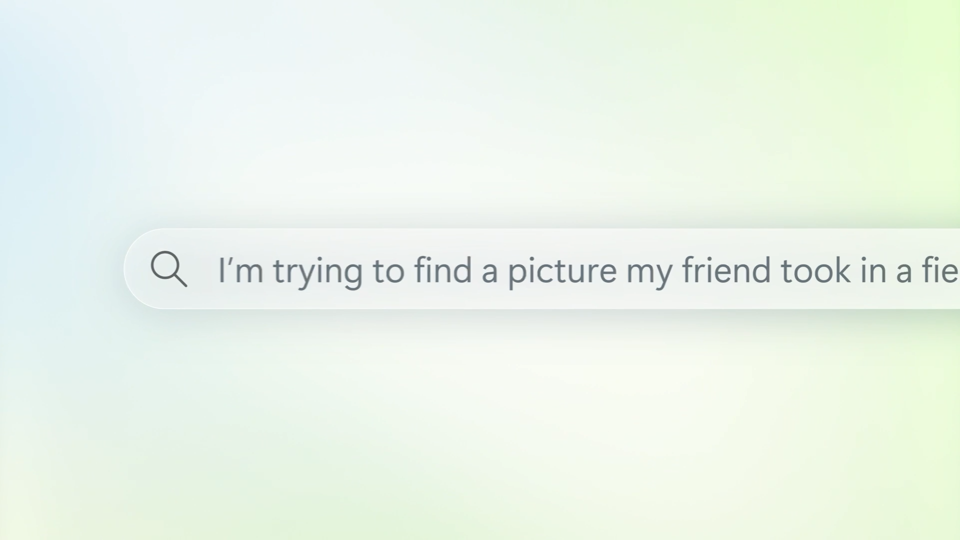 A search bar with text that reads, “I’m trying to find a picture my friend took in a fie.” The background is softly blurred in pastel green and blue tones.