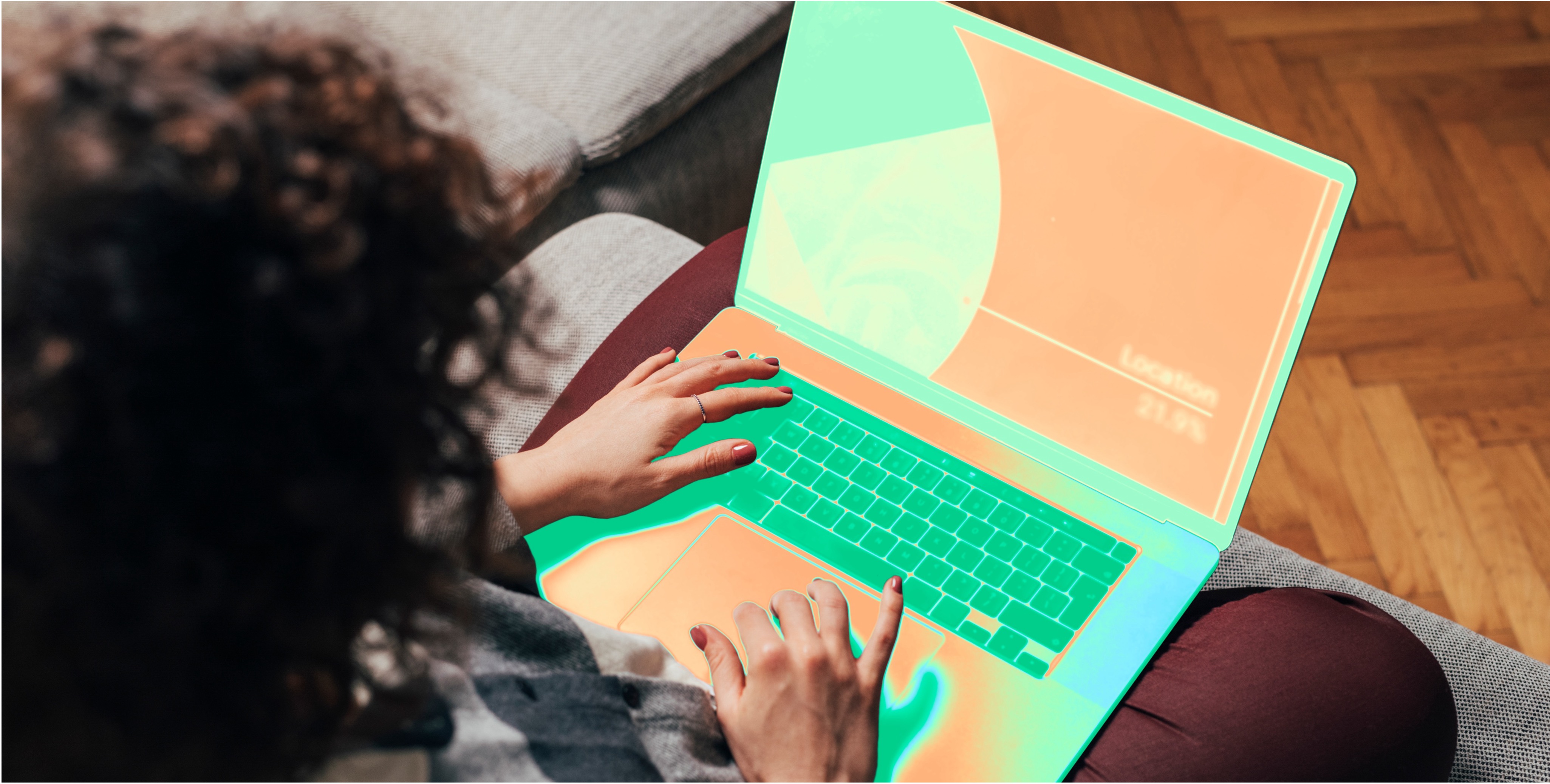 A person with curly hair is sitting on a couch, using a laptop. The screen displays a presentation slide with the title "Location" and some charts or graphics. The person's hands are on the keyboard and trackpad.