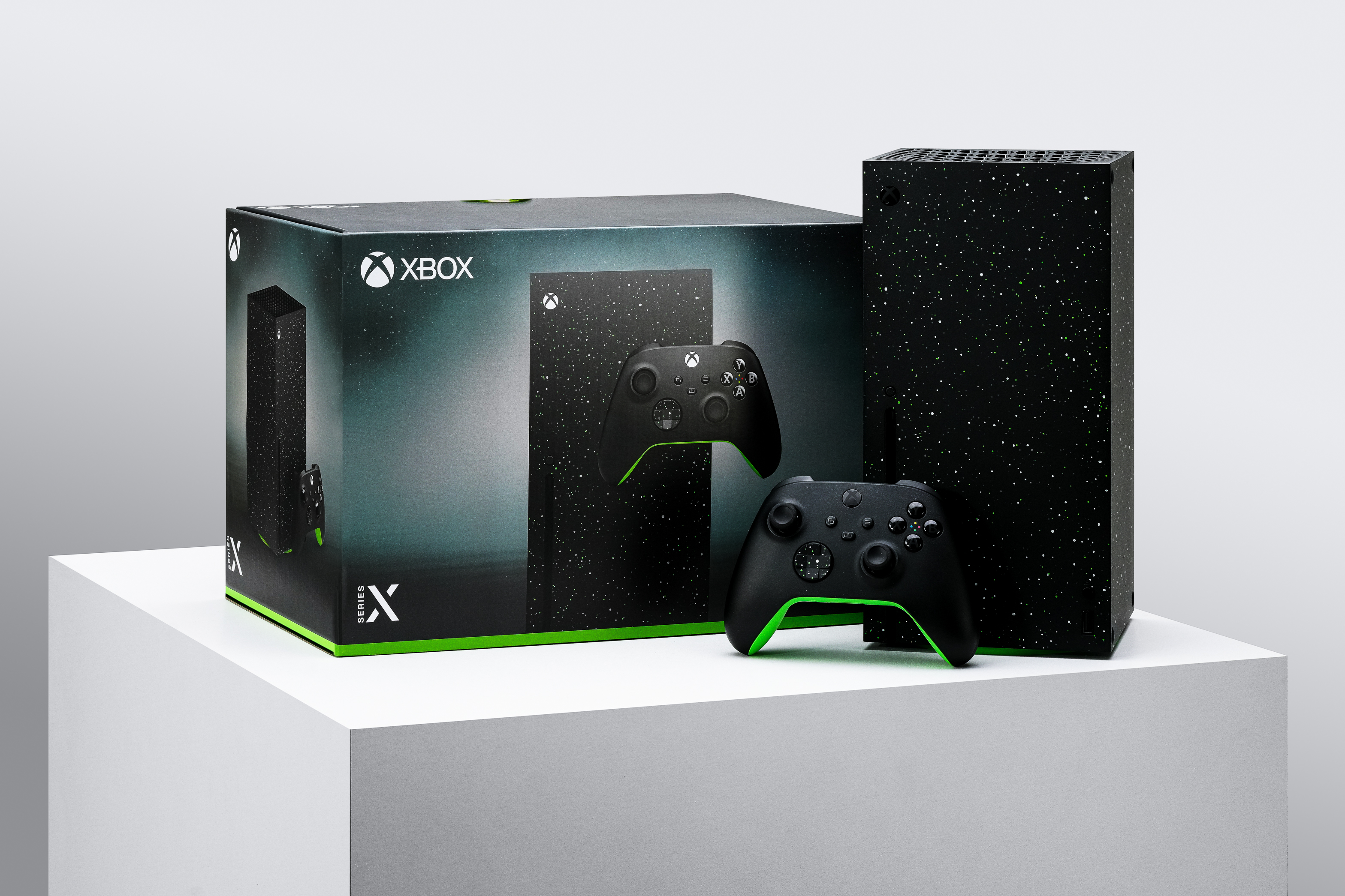 A special edition Xbox Series X console and controller with a speckled, starry design are displayed next to their matching box on a white pedestal against a light gray background.