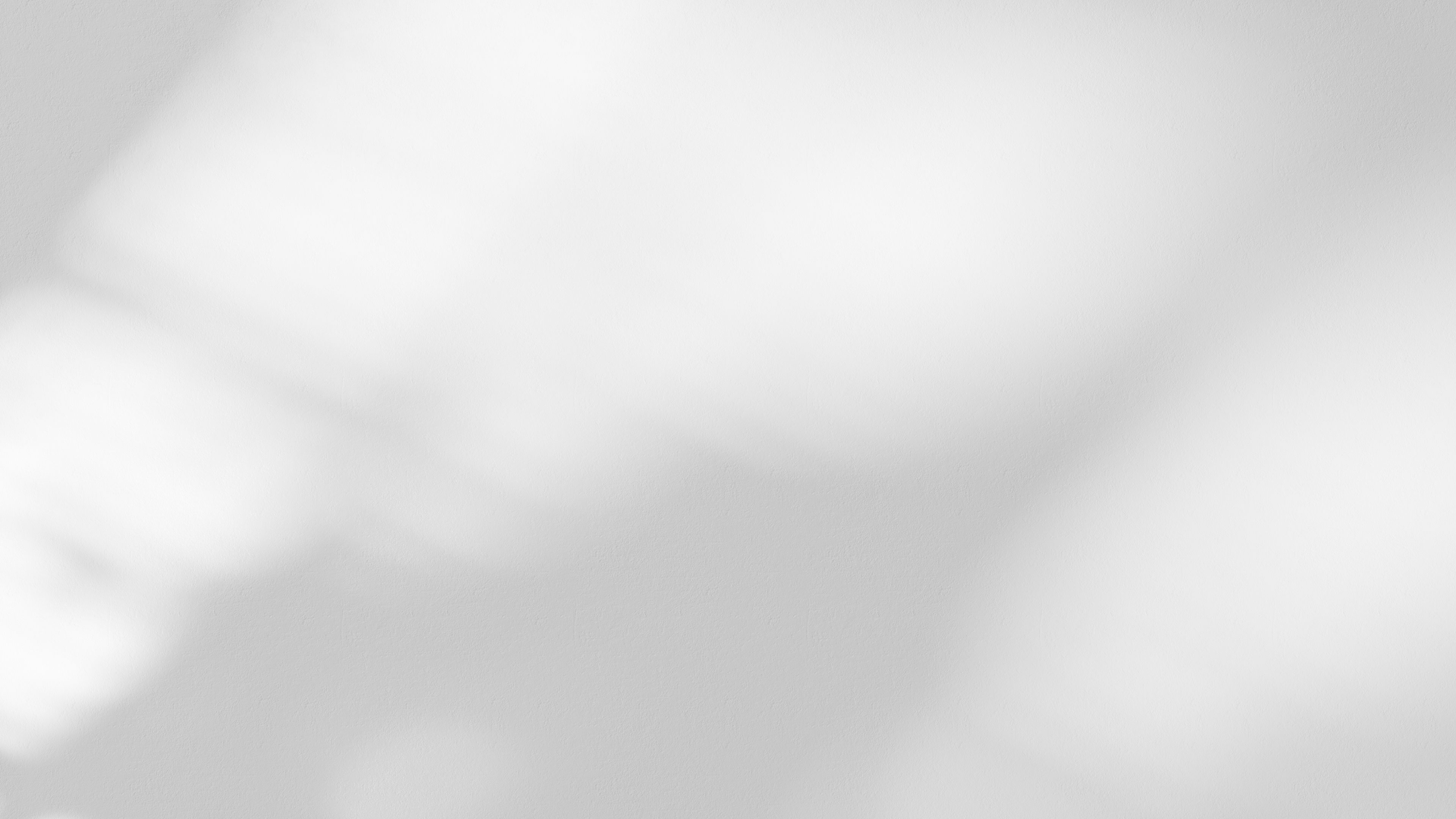 A blurred, abstract image with soft white and grey tones. Light appears diffused across the surface, creating a gentle, minimalistic pattern with no distinct objects or shapes visible.