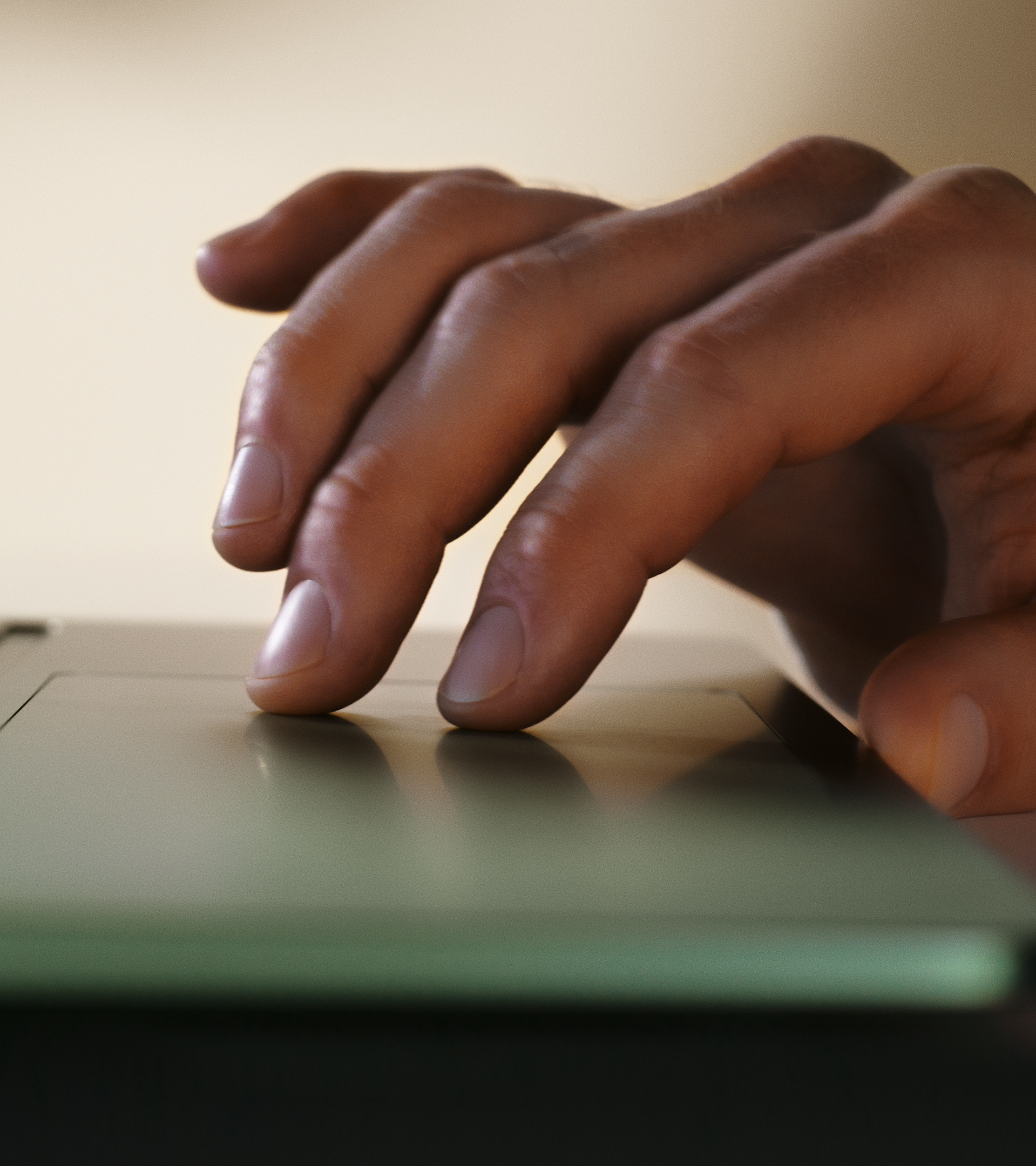 A close-up of a person's hand using a laptop trackpad, with fingers resting gently on the smooth surface, suggesting navigation or interaction with the device.