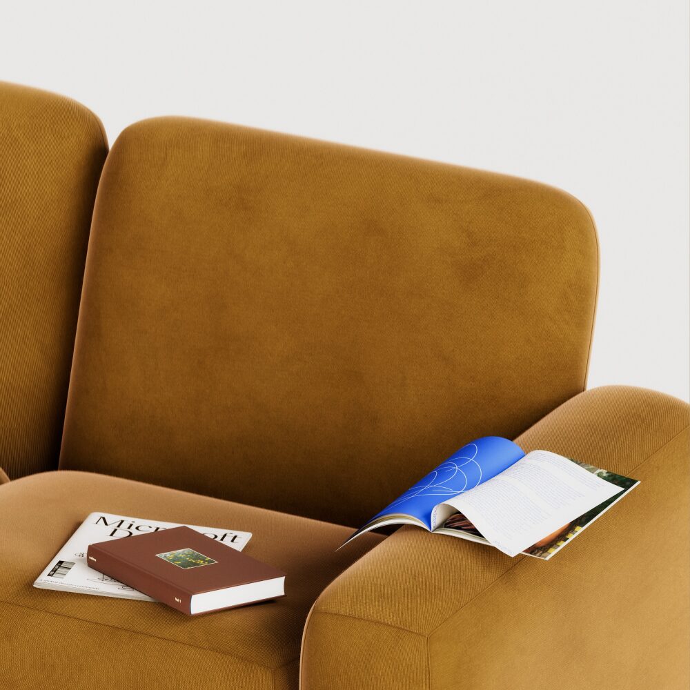 A brown couch with a closed brown book, a magazine, and an open blue magazine resting on its seat and armrest against a white background.