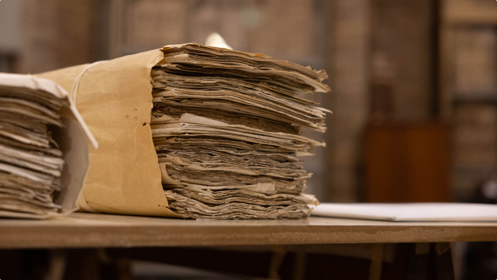 A stack of old, worn documents bound in a tan paper folder on a wooden surface.