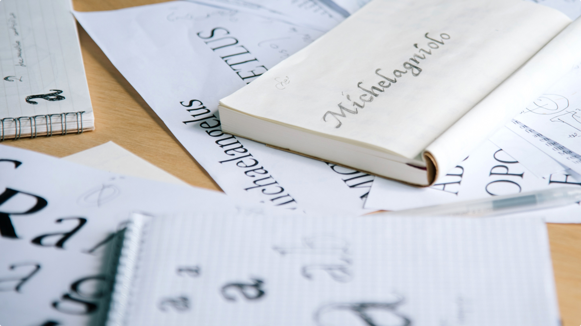 Notebooks and loose papers covered in hand-lettered calligraphy sketches, including the name “Michelagniolo.”